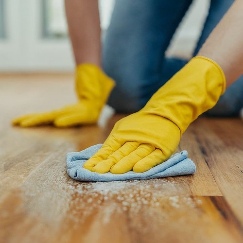 The image shows a Mold on Wood Floors close-up of a wooden floor with significant mold growth. The mold appears as dark, fuzzy patches spread across the wood grain. The color of the mold varies from black to dark green. There are also visible signs of water damage, with the wood warping and discoloring in some areas.