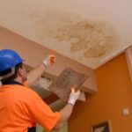 Worker inspecting and repairing water damage caused by a leak in ceiling, showing visible stains and discoloration on the surface