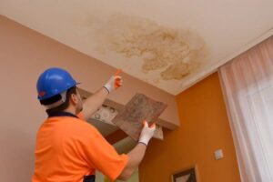 Worker inspecting and repairing water damage caused by a leak in ceiling, showing visible stains and discoloration on the surface