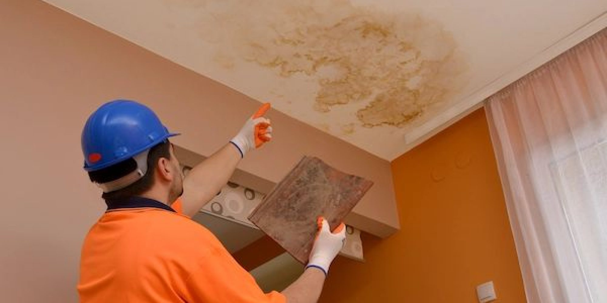 Worker inspecting and repairing water damage caused by a leak in ceiling, showing visible stains and discoloration on the surface
